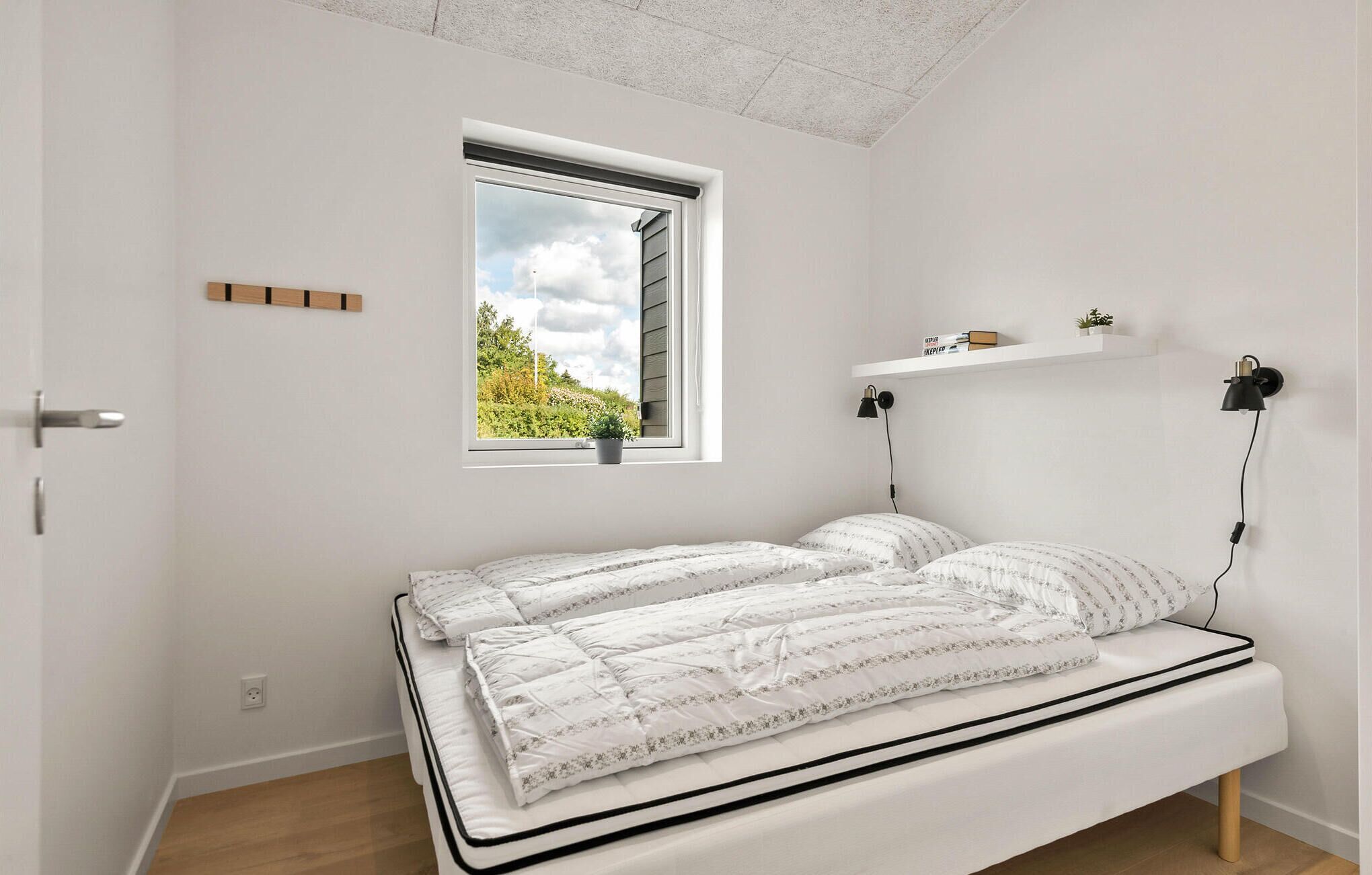 A bedroom with a bed, a window, a shelf, and a door.