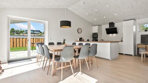 Una cocina moderna con una isla central, un comedor con mesa de madera y sillas grises, y un amplio ventanal corredera que da a un patio trasero.