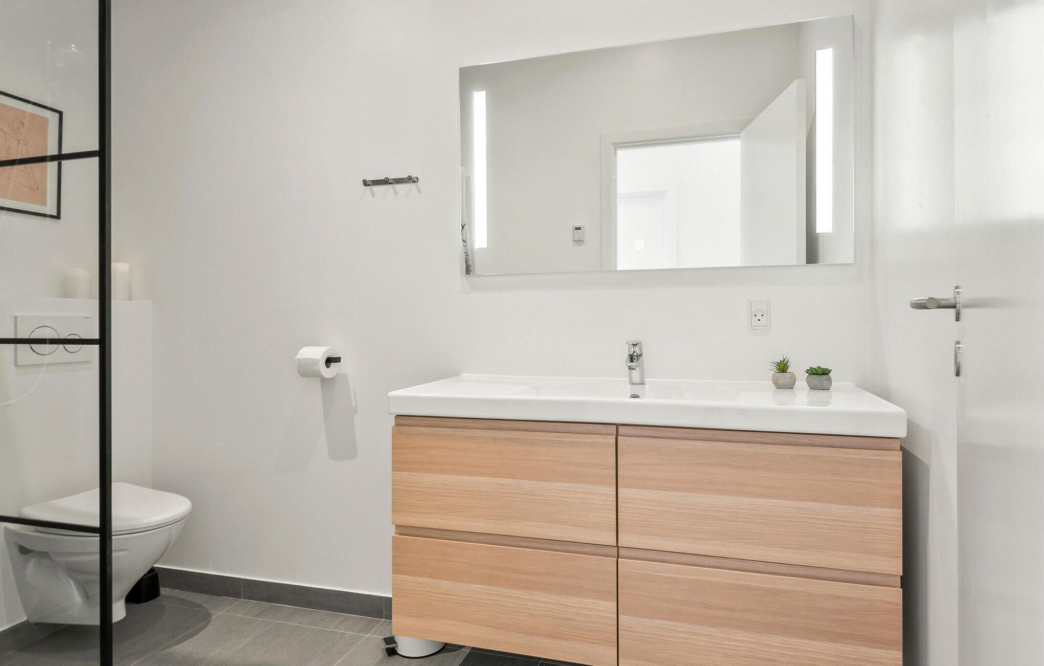 Een moderne badkamer met een witte wastafel, een houten opbergmeubel en een grote spiegel.