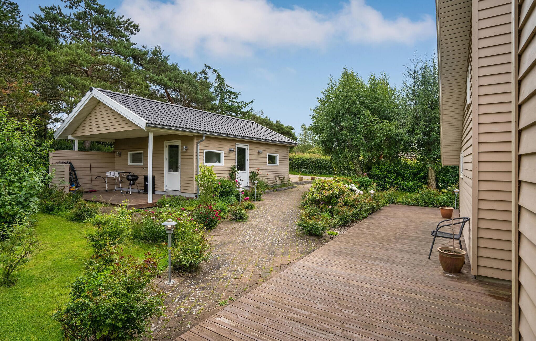 Een gelijkvloers huis met een overdekte veranda, omgeven door een tuin met diverse planten en bloemen.