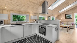 Une cuisine moderne avec des meubles blancs, un four encastré et une grande fenêtre donnant sur un paysage verdoyant.