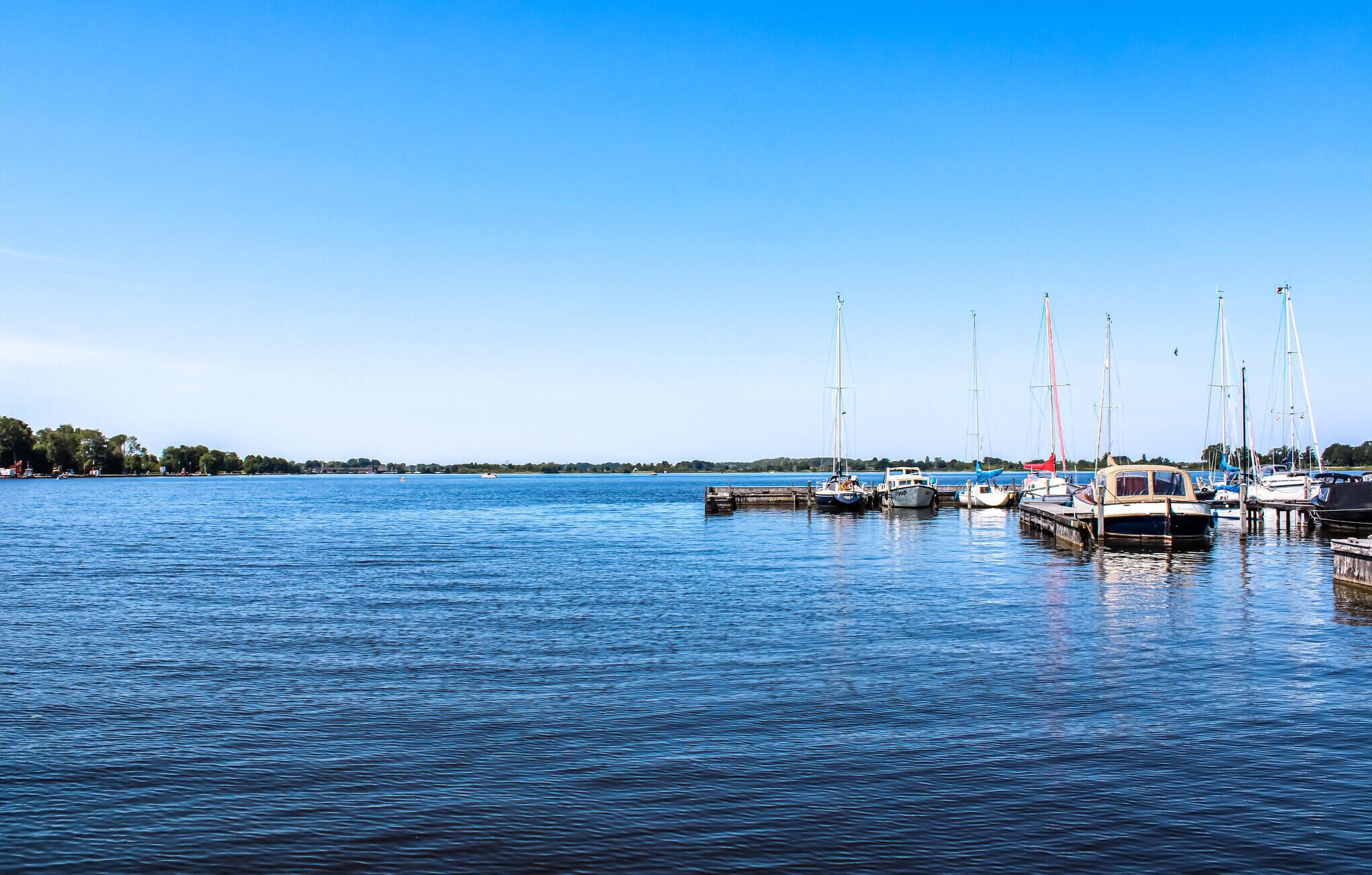 A marina with several boats docked, calm water, and a clear sky.