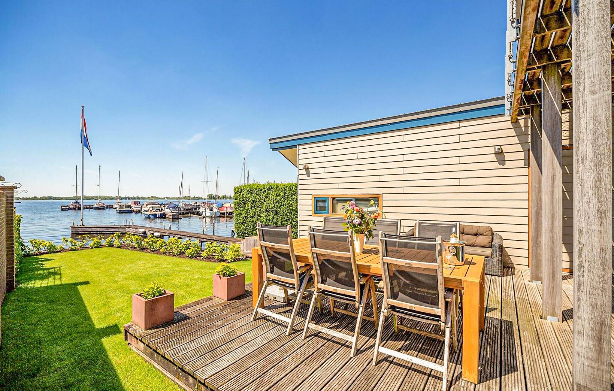 Ein Ufergrundstück mit Holzterrasse, Sitzgelegenheiten im Freien und Blick auf Boote und eine Flagge.