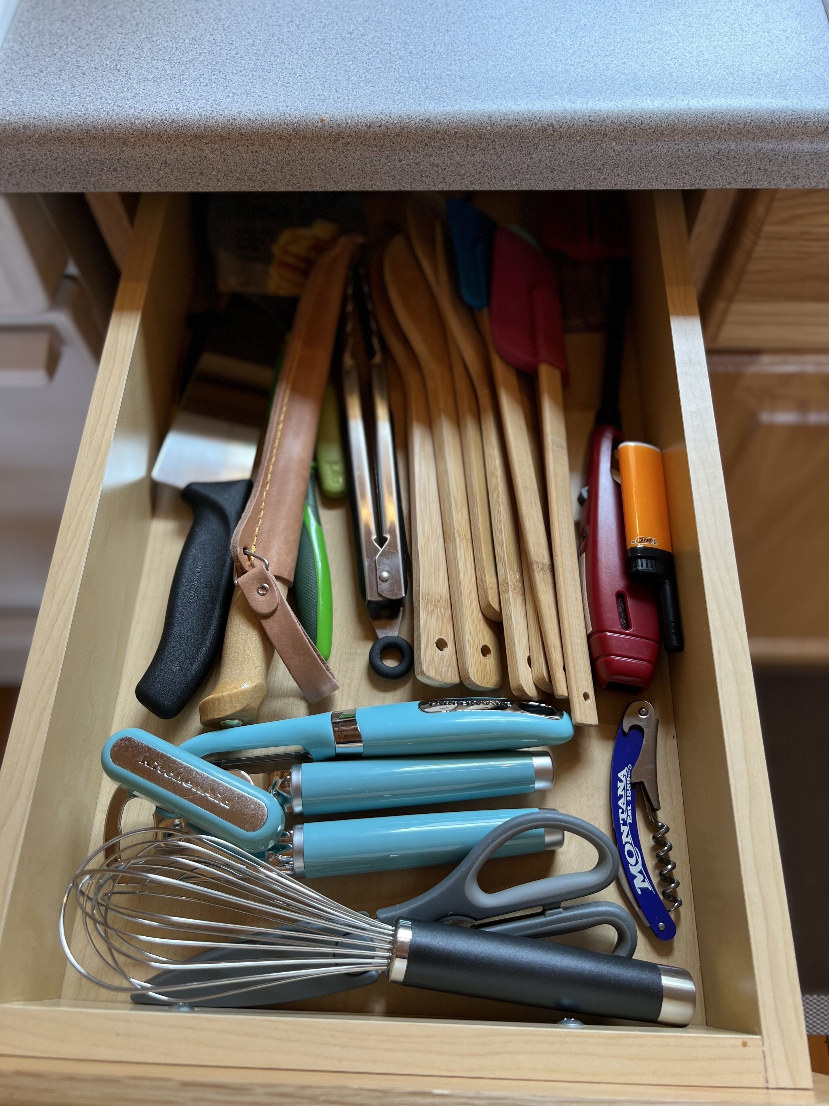 A drawer with various kitchen utensils including whisks, knives, and a can opener.