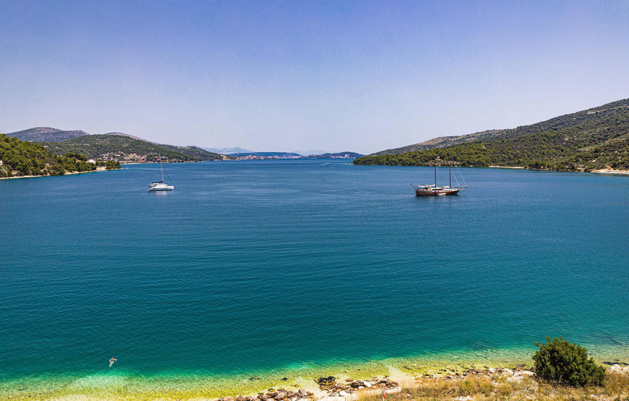 Una baia tranquilla con due barche a vela ancorate, circondata da colline e acque cristalline.