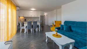 Una sala de estar moderna con un sofá azul, una mesa de centro blanca y un comedor con una mesa y sillas blancas.