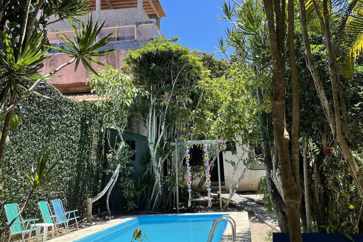 A pool area with blue lounge chairs and a small table, surrounded by tropical plants and trees.