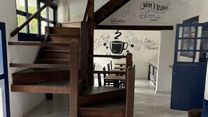 A spacious living area with a wooden staircase, a sofa with patterned cushions, and a dining table. - Pousada Bicho do Mar (Arraial do Cabo)