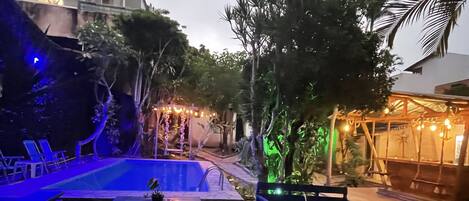 Zona de piscina exterior con cubierta de madera, sillas de descanso y mesas.