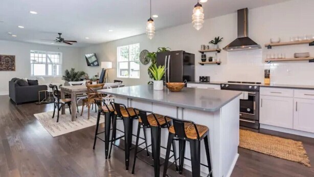 Una cocina moderna con una isla central, taburetes de bar y un comedor con sofá y sillas.