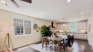 Una sala de estar amplia con un gran ventanal, un comedor con una mesa y sillas de madera, y una cocina con armarios blancos y una isla central.