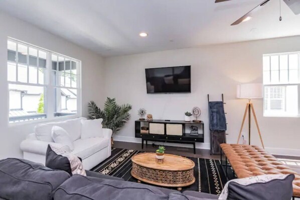 A living room with a white sofa, a grey sofa, a coffee table, a TV mounted on the wall, and a floor lamp.