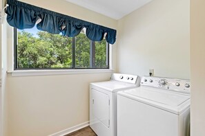 A laundry room with a washer and dryer, a window with a view of trees, and a wall-mounted control panel. - Walk to Coligny Beach & Plaza, 2 Pools Steps Away, Sleeps 6 (Hilton Head Island)