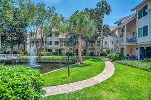 A courtyard with a fountain, surrounded by well-maintained lawns and palm trees, with multi-story buildings in the background. - Steps From Pool, Walk to Coligny, Close to Beach, Hilton Head, Courtside Villas  (Hilton Head Island)