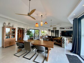 Amplia sala de estar con una mesa de comedor de madera, sillas modernas, un televisor grande y ventiladores de techo.
