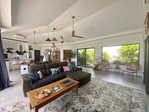 Amplia sala de estar con un sofá grande, una mesa de centro y vistas al exterior a través de grandes ventanales.