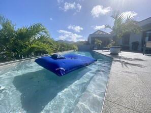 Una piscina cristalina con una silla hinchable azul y palmeras.