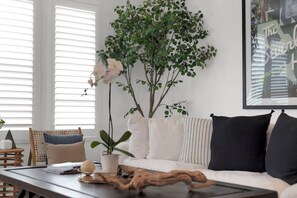 Un saló amb un sofà blanc, una taula de centre amb un element decoratiu de fusta i una planta verda gran.