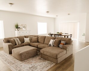 Una sala de estar con un sofá modular, una mesa de comedor con sillas, una mesita auxiliar y una escalera.