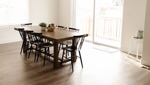 Comedor con mesa y sillas de madera, una planta en maceta y vista a un balcón con barandilla de madera.