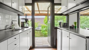 Une cuisine moderne avec des meubles blancs, des plans de travail en acier inoxydable et une vue sur un jardin, accessible par une porte ouverte.