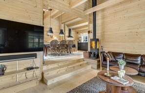 A cozy wooden cabin interior with a TV, dining area, fireplace, and leather sofa. - 4 bedroom amazing home in Nexø (Nexø)