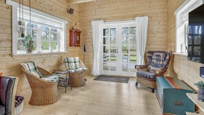 L’intérieur chaleureux d’un chalet, avec des meubles en osier, un plancher en bois et de grandes fenêtres offrant une vue sur l’extérieur.