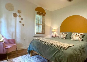 A bedroom with a bed, a chair, a window with blinds, and wall decor.