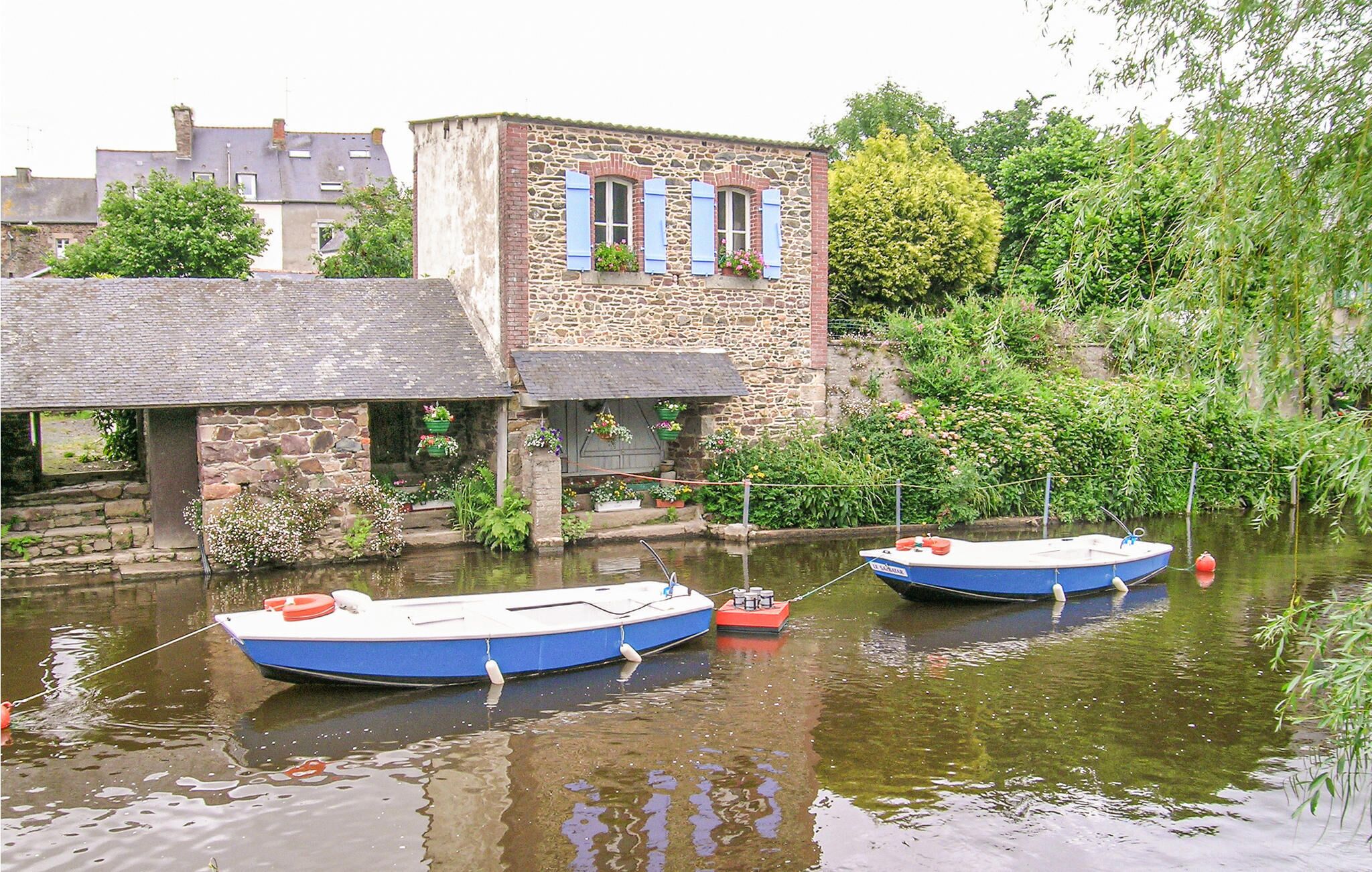 Deux bateaux étaient amarrés à un bâtiment situé au bord de la rivière, un bâtiment aux murs de pierre et aux volets bleus.
