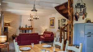 Un comedor con una mesa de madera preparada para cuatro personas, rodeada de sillas blancas. Se aprecia un sofá rojo y un aparador de madera al fondo.
