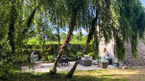 Un jardín con mobiliario de mimbre, una silla colgante y una pared de piedra.