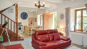 Amplia sala de estar con un sofá de cuero rojo, un comedor con muebles de madera, un gran reloj de pared y vistas a zonas verdes a través de una ventana.