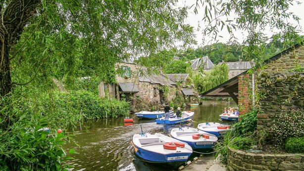 Un canal estrecho con barcos amarrados a sus orillas, rodeado de abundante vegetación y edificios históricos de piedra.
