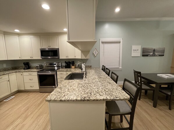 A modern kitchen with white cabinets, granite countertops, stainless steel appliances, and a dining area with a table and chairs. - Cozy riverfront cottage with an amazing view, minutes from downtown New Bern. (Bridgeton)