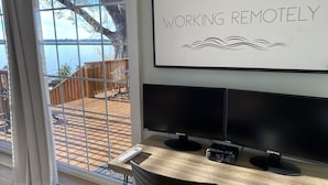 Un bureau à domicile doté d’une grande fenêtre donnant sur une terrasse et un lac, avec une pancarte indiquant : « TRAVAIL À DISTANCE ».