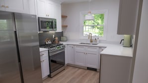 Una cocina moderna con armarios blancos, electrodomésticos de acero inoxidable y un ventanal que proporciona luz natural.