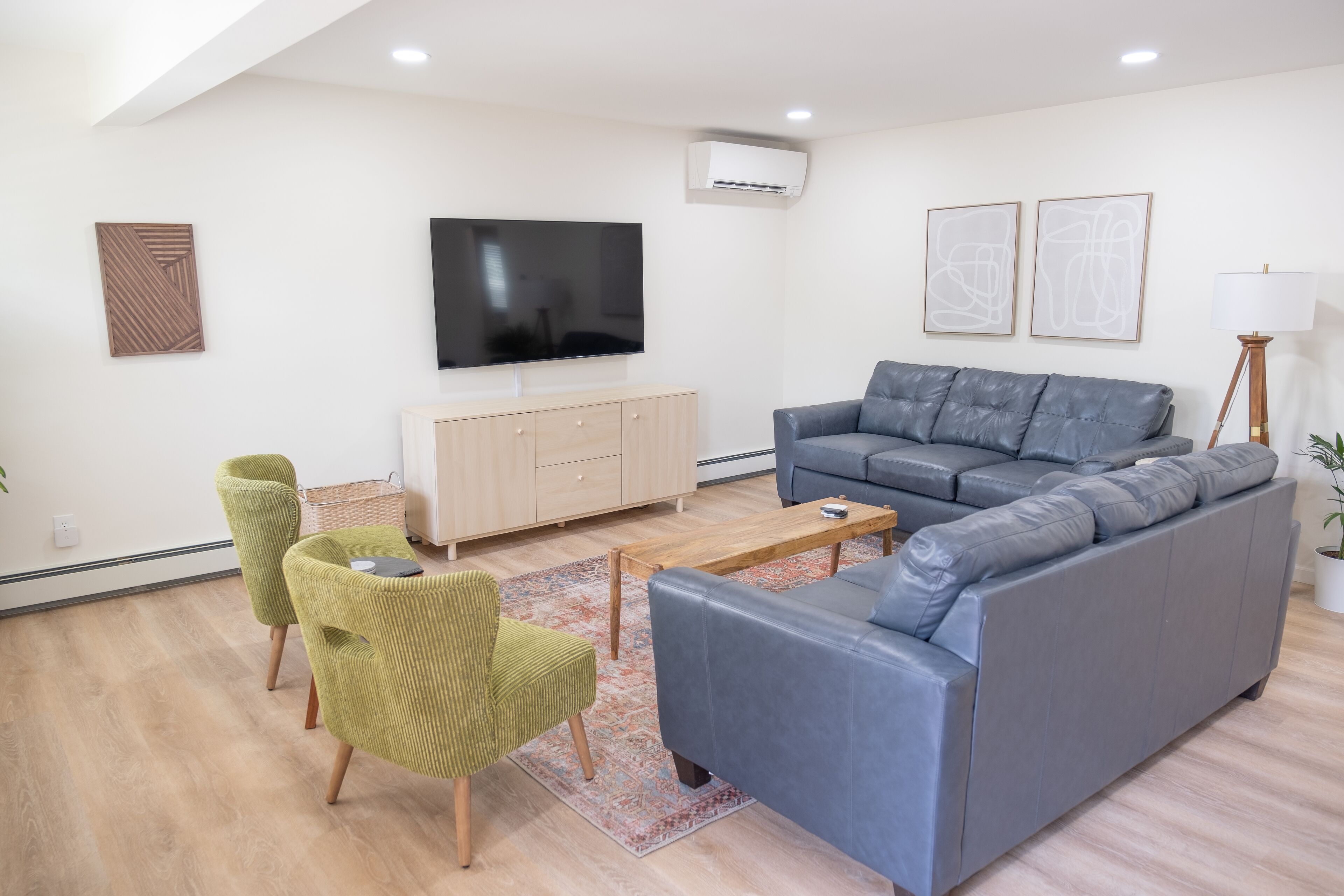 Un salon moderne avec un canapé gris, des fauteuils verts, une table basse en bois et un téléviseur à écran plat fixé au mur.