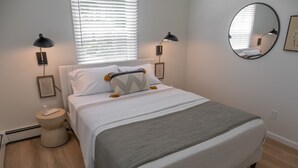 Un dormitorio ordenado con cama, lámparas de noche, un espejo redondo y un cuadro en la pared.