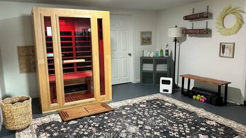 Una habitación con un gran armario de madera, una alfombra con estampado blanco y negro, un pequeño calentador blanco, un banco, una lámpara y un estante de pared con adornos.