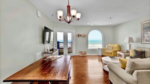 Un salón amplio con una mesa de comedor de madera, un sofá y un sillón amarillo. Un ventanal ofrece vistas al océano.