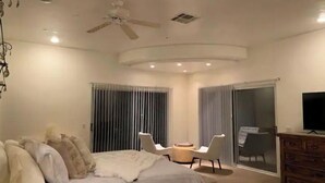 Une chambre à coucher moderne, équipée d’un lit, d’un ventilateur de plafond, d’une télévision et d’une porte-fenêtre coulissante donnant sur un balcon.