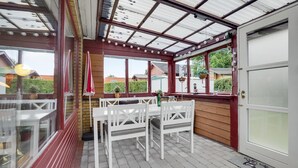 Een overdekt terras met witte stoelen en tafels, een houten terras en uitzicht op de omgeving.
