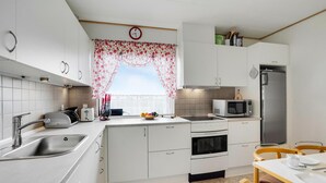 Een kleine keuken met witte kastjes, een roestvrijstalen spoelbak, een magnetron, een oven en een koelkast.