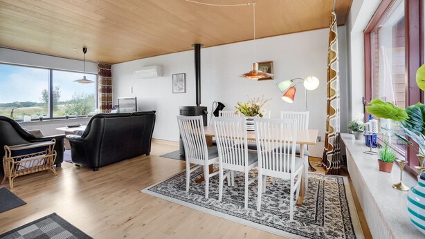 Een moderne woonkamer met een eethoek, met een groot raam, een zwarte bank, witte stoelen en een tafel met een bloevas.