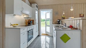 A modern kitchen with white cabinets, a built-in oven, a sink, and a window overlooking a garden. - Cozy home in Hurup Thy with sauna (Hurup Thy)