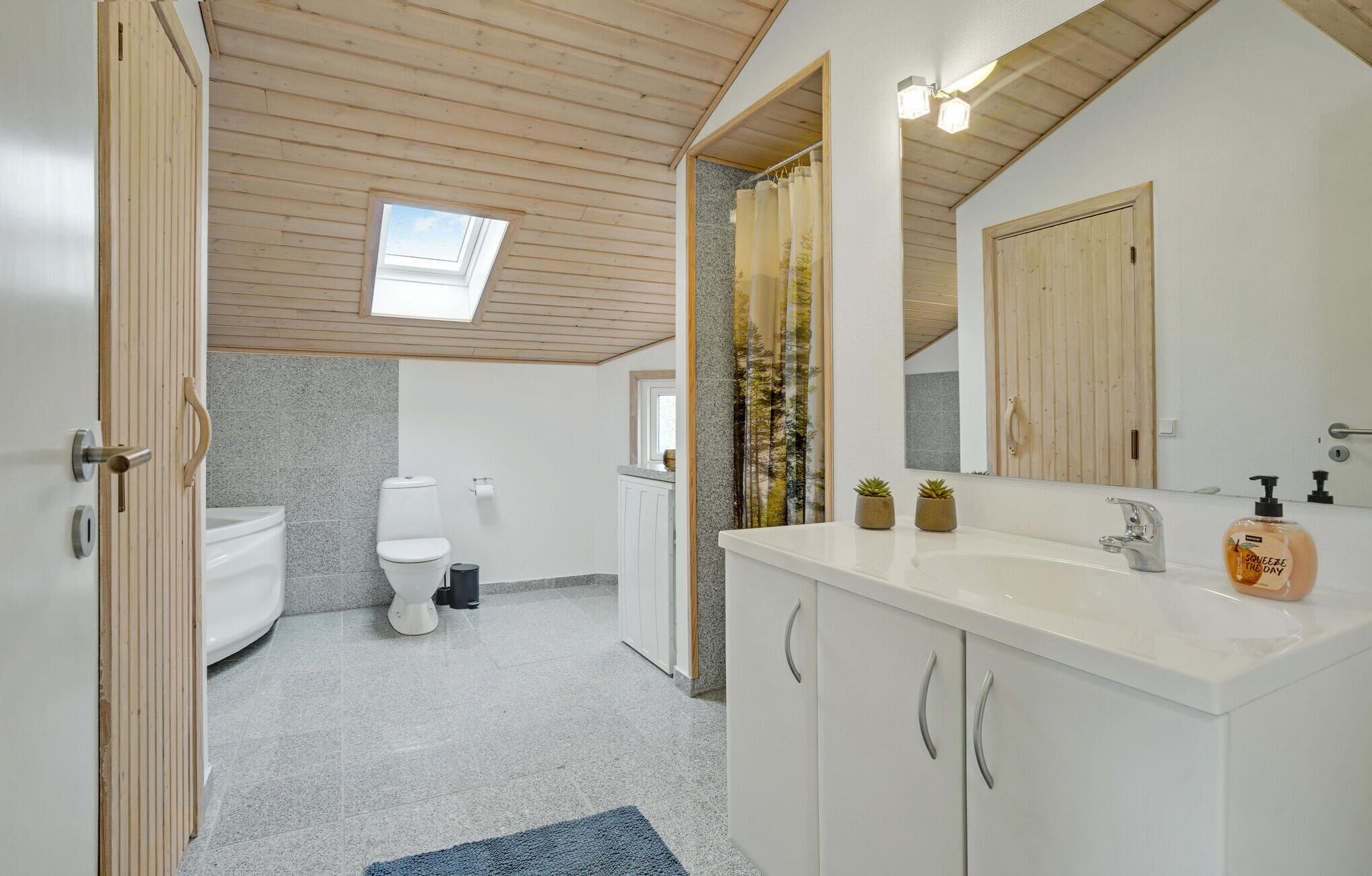 Et moderne badeværelse med ovenlys, toilet, vask med spejl og træskabe.