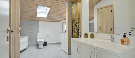 Et moderne badeværelse med ovenlys, toilet, vask med spejl og træskabe.