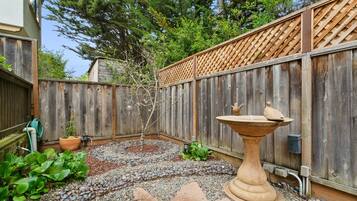 Enjoy a serene outdoor space with a bird bath, potted plant, and small tree surrounded by a rustic fence.