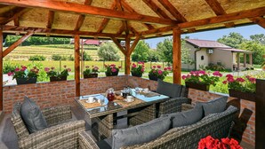 Un espace extérieur aménagé en terrasse, avec des meubles en osier, une table dressée avec des tasses et une théière, et des plantes en pot.