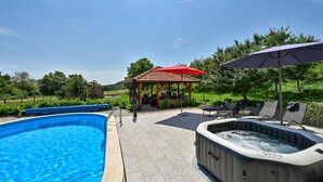 Une piscine, un jacuzzi, des chaises longues et un kiosque agrémenté d’un parasol rouge.